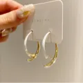 Detail view of minimalist gold and white curved hoop earrings on a presentation card. - White Enamel