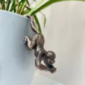 Gros plan d'une figurine de singe en résine bronze accrochée à un pot de fleurs gris, déco. - Singe