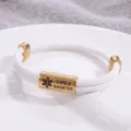 Vista dettagliata del bracciale medico intrecciato bianco con tubo inciso in oro. - Stile Allerta Medica / Corda Bianca Hardware Dorato