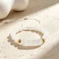 Nahaufnahme des weißen Perlenarmbands mit goldenen Perlen und einem zentralen Brückenanhänger. - Opalith Armband
