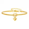 Close-up van de gouden slangenketting armband met hartvormige hanger en een sierlijke knoop. - Goud