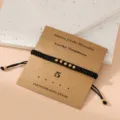 Black braided Morse code number bracelet with gold beads on card, minimalist style jewelry. - Morse Code 5 Black Flat Knot Cord Bracelet with Card