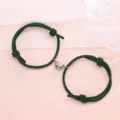 Detail view of magnetic couple bracelets featuring dark green braided cords and half heart alloy charms. - Minimalist Dark Green Pair