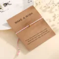 Detailed close-up view of a colorful braided cotton cord wish bracelet with a gold bead on card. - Lake Blue (F2)