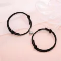 Detailed view of black braided couple bracelets featuring a magnetic metal heart clasp design. - Minimalist Black Pair