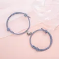 Close up detail of couple magnetic heart bracelet featuring blue woven cord and alloy charm. - Minimalist Gray Pair