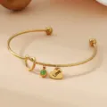 Gros plan detaille du bracelet en acier dore avec cristal vert et pendentif coeur. - Or / Pierre de Naissance d'Août