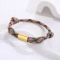 Detailed shot of a braided rope bracelet with a gold metal tube clasp on white tray. - Green, Black and Pink Paracord