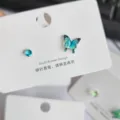 Nahaufnahme der asymmetrischen blauen Schmetterling- und Kristall-Ohrstecker auf der weißen Karte. - Seeblauer Schmetterling