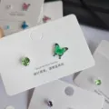 Nahaufnahme der bunten Schmetterlings- und Kristall-Ohrstecker auf weißer Displaykarte. - Grüner Schmetterling