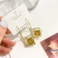 Nahaufnahme geometrischer quadratischer Ohrringe mit gelben Kristallen und funkelnden Steinen. - Champagner