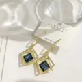 Detailaufnahme geometrischer Goldohringe mit blauem Kristall und Strass auf Karte elegant. - Blau