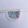 Mini floral doll apron accessory with white ruffle trim and delicate ribbon string. - Purple Garden Bib
