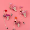 Close-up of handmade crochet mushroom keychains with colorful pom poms on pink background - Pink