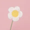 Close-up of a handmade crocheted white and yellow yarn daisy flower on a light pink background - White