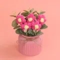 Detail von handgefertigten rosa Häkelblumen in einem strukturierten rosa Topf mit Juteband - Fuchsia