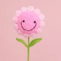 Detailed view of a hand-crocheted pink smiling flower with green stem and leaves. - Pink 7 Rings Smiley Face Bouquet