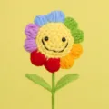 Close-up detail of a handmade rainbow crochet sunflower with a cute smiley face - Multicolor Smiley Face 5 Rings With 2 Leaves