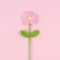 Detailed view of hand-crocheted pink puff flower with green leaves on pink background - Large Puff Flower (Double Leaf) / Pink