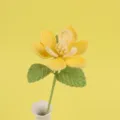Close-up of a handmade yellow crocheted magnolia flower with green leaves in a white vase - Yellow