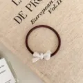 Close-up view of a brown elastic hair tie with a white bow charm on fabric. - Ribbon Style / Pearl White