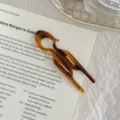 Close-up view of a tortoise shell acetate fish hair pin resting on an open book page - Caramel Lines - Large