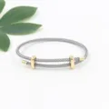 Primer plano de una pulsera de cable de acero gris ajustable con piezas doradas - Gris Plateado