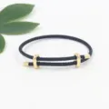 Detailed view of adjustable black braided bracelet with a gold-tone figure-8 buckle. - Black