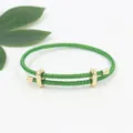 Vista detallada de la pulsera de cable trenzado verde con hebillas doradas ajustables. - Verde