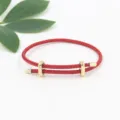 Detailed view of an adjustable red braided wire rope bracelet featuring gold infinity buckles. - Red