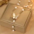 Nahaufnahme-Makrodetail einer eleganten goldenen Schmetterlingskette mit weißen Perlen - Schmetterling Muschel Anhänger / Gold