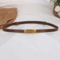 Dettaglio della sottile cintura in pelle marrone con fibbia metallica dorata elegante. - Colore caramello