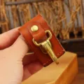Closeup of brown leather key holder detail with brass hook and snap button for belt accessories. - Khaki