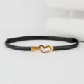 Close-up detail view of the thin black leather waist belt featuring a stylish gold heart buckle. - Black