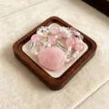 Makroansicht eines rosa Kristallarmbands mit Blumenschnitzerei auf einem Holztablett - Rosenquarz Neunschwänziger Fuchs Stil (Kuan Er)