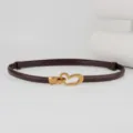 Close-up detail of the elegant dark brown thin leather belt with gold heart buckle. - Coffee