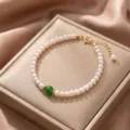 Elegant close-up of a natural white pearl bracelet with a green gemstone on a satin display box - Style 7