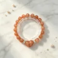 Nahaufnahme eines eleganten orangefarbenen Sonnenstein-Perlenarmbands auf Marmor - Herzanhänger-Armband (Stil 23)