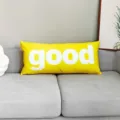 Vista detallada del cojín decorativo amarillo largo con texto good blanco en sofá gris. - DAJS06