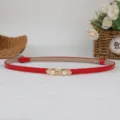 Cintura sottile in vernice rossa con fibbia dorata di perle, scatto di dettaglio per donna. - Rosso