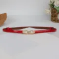Primo piano dettagliato della sottile cintura in ecopelle rossa con fibbia dorata. - Rosso