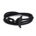 Detalle en primer plano de la pulsera de cuerda trenzada negra con un dije de cola de ballena. - Negro
