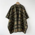 Vista detallada de un poncho de punto verde oscuro con un elegante diseño de lunares. - Verde con flor amarilla