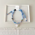 Close-up detail van blauwe stoffen sterrenbeeld ketting met houten kralen en strandstijl. - 02 Zeester - penseelbloemen blauwe basis