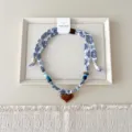 Detailopname van blauw-witte stoffen lintketting met kleurrijke kralen en hartvormige hanger. - 07 Hart - tien-raster stip bloemen gebroken wit