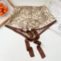 Detail shot of the stylish paisley silk scarf with pearl magnetic buckle and ribbon ties. - Pearl Buckle - Paisley Yellow