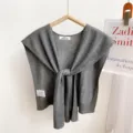 Close-up detail of grey knitted small cape shawl showing front knot design and brand label. - Dark Gray