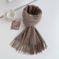 Detailed shot of a cozy brown solid winter tassel imitation cashmere scarf on clean white table. - Dark Velvet