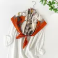 Detail view of the elegant satin silk square scarf featuring a retro carriage and tassel print. - Orange Carriage