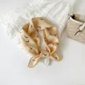 Detail van een beige zijden vierkante sjaal met minimalisten vogelprint, chic haar- en nekaccessoire. - Geel